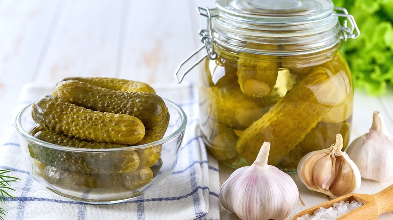 A glass bowl and Mason jar full of pickles