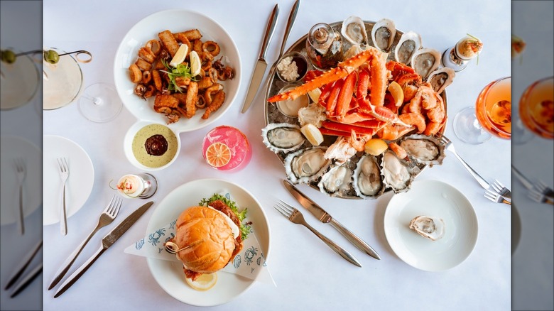 Three seafood dishes on white cloth table with drinks and silverware