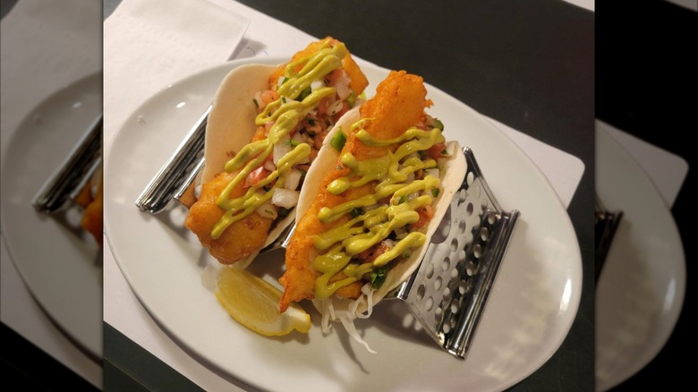 Battered fish tacos with green sauce on metal taco holder
