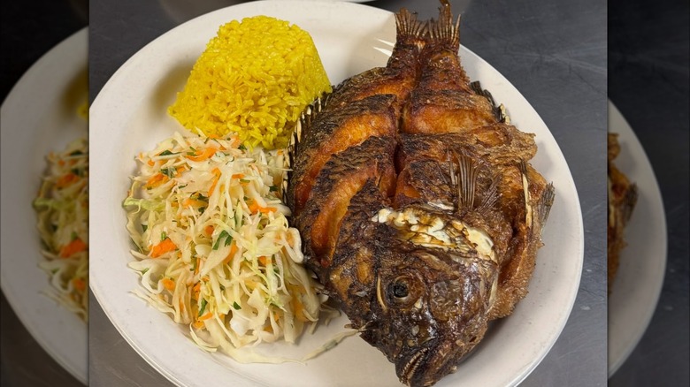 Whole fish grilled on white plate with coleslaw and yellow rice