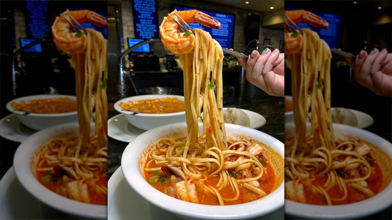 Fork holding prawn and noodles out of bowl