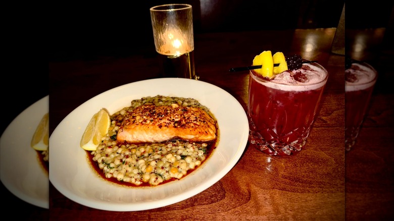 Salmon on a bed of pasta next to a cocktail