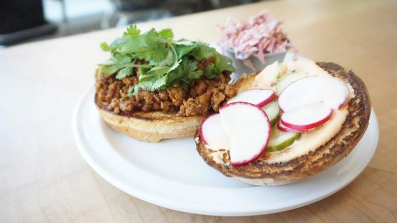 dollop diner open face sloppy joe with fresh leafy herbs, radish slices, and sauce on toasted white bun