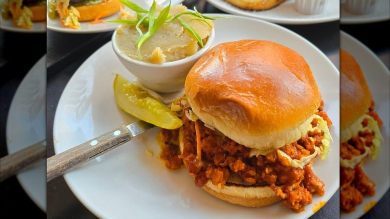 Handlebar sloppy joe on white plate with pickle and side of mashed potatoes