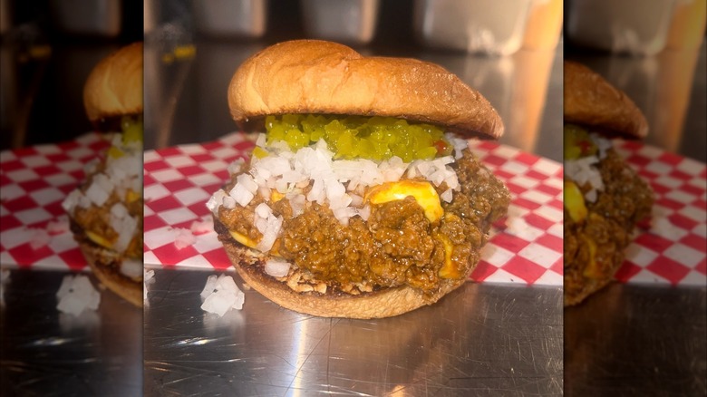 Sloppy buns' sloppy joe on bun with onions and relish on metal counter
