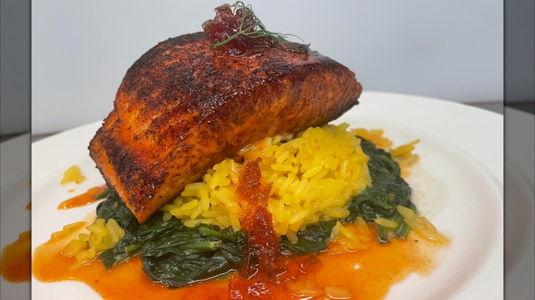 Heard Dat Kitchen blackened salmon atop yellow rice, collard greens, and red sauce on white plate