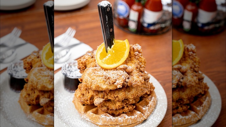 Chicken and waffles topped with powdered sugar and lemon on plate with knife