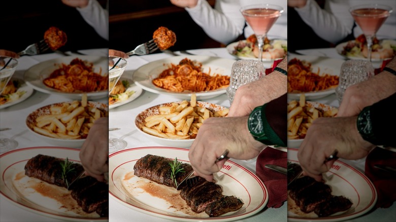 Hands cutting into a steak on a table with other dishes