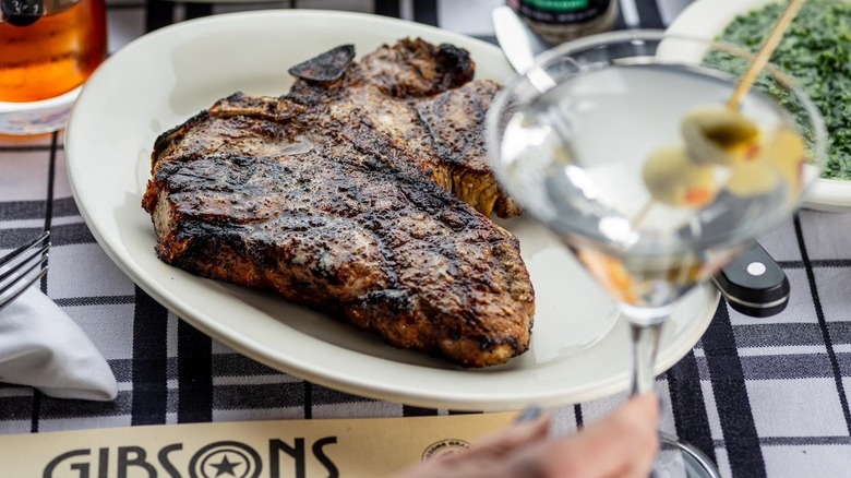 A table set with a plate of steak and a martini in the forefront