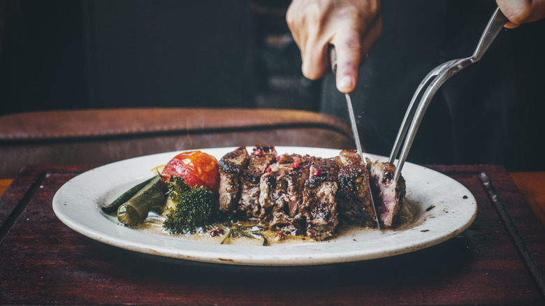 A piece of steak being carved into slices on a plate
