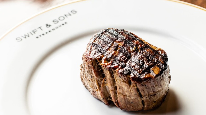 A piece of steak served on a white plate embossed with Swift & Sons Steakhouse