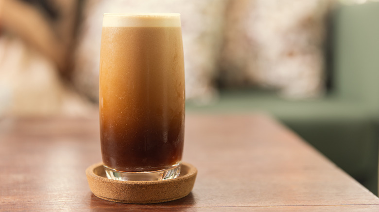 A foamy cup of nitro brew coffee on a solid dark-colored surface.