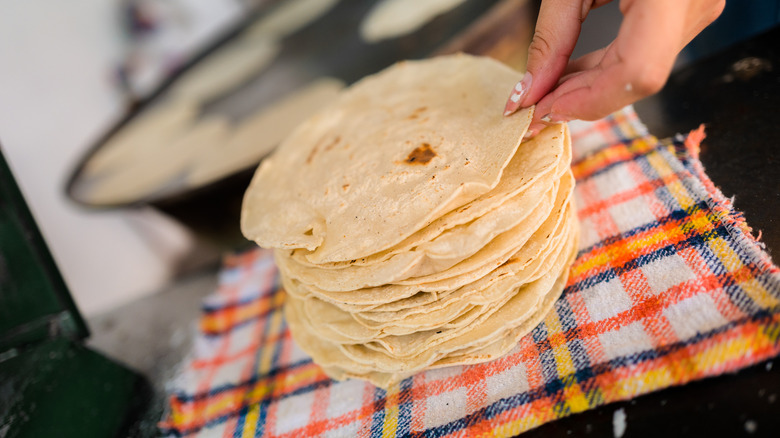 A hand stacking corn tortillas on a checkered cloth
