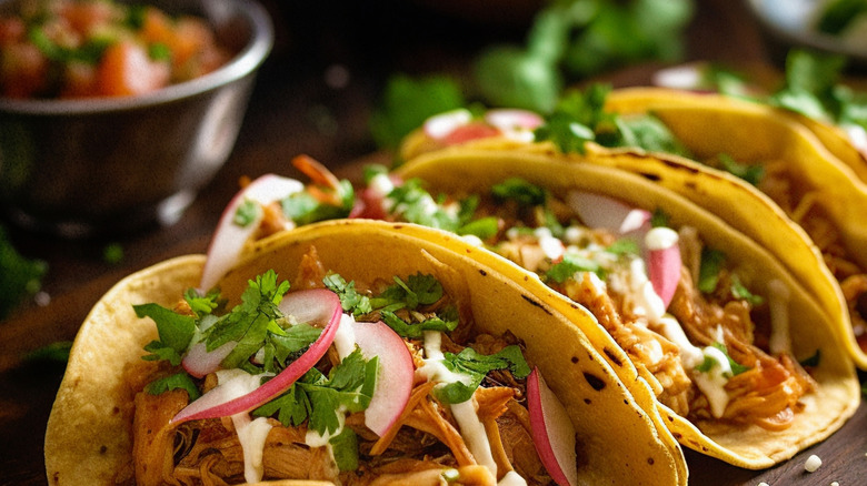 A row of chicken street tacos topped with sour cream, radish, and cilantro