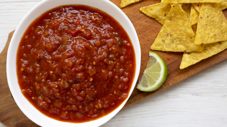 A bowl of salsa with chips on a wood platter