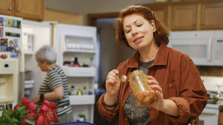 A woman uses a spoon to get salsa out of a large jar