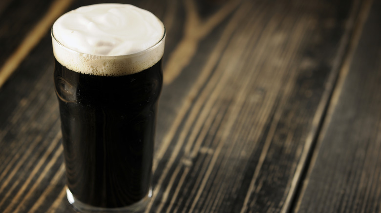 Dark beer in a glass with a small amount of foam on top on a wooden surface