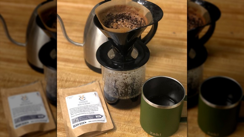 A mug, a coffee maker, and a coffee packet positioned on a table
