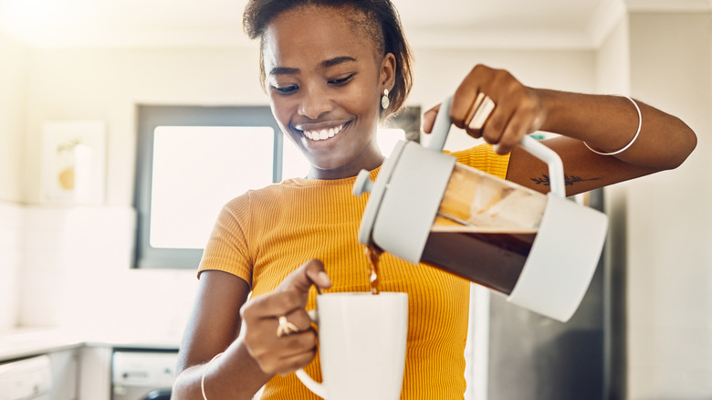 A short-haired woman in a yellow t-shirt pouring coffee