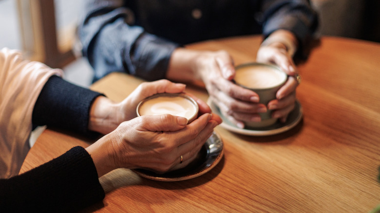 Two people holding full mugs of coffee