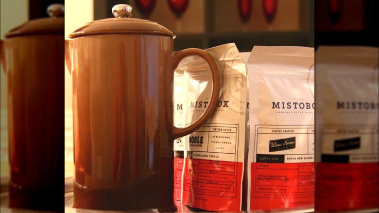 A brown coffee pot positioned next to a few bags of Mistobox coffee