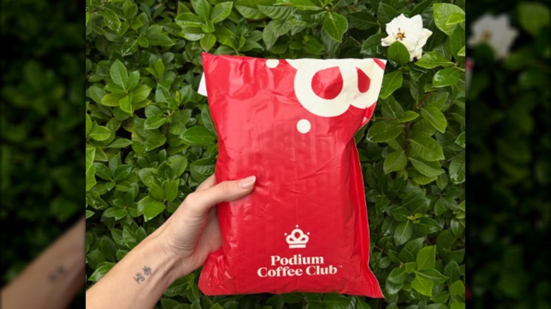 A hand holding a red Podium Coffee Club package