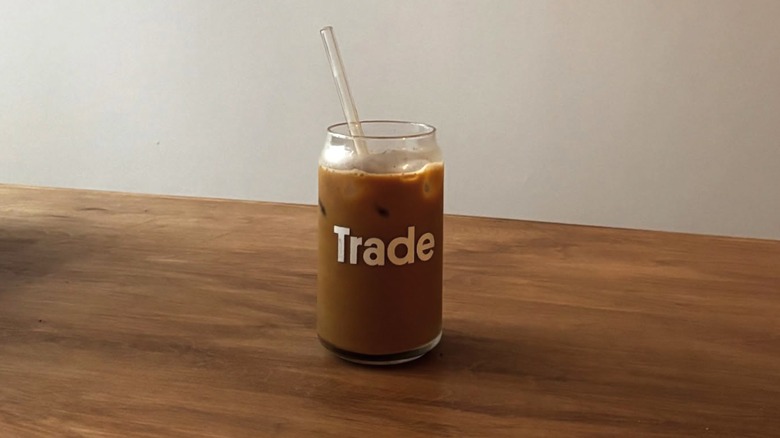 A clear, coffee-filled glass labeled "trade" positioned on a wooden counter