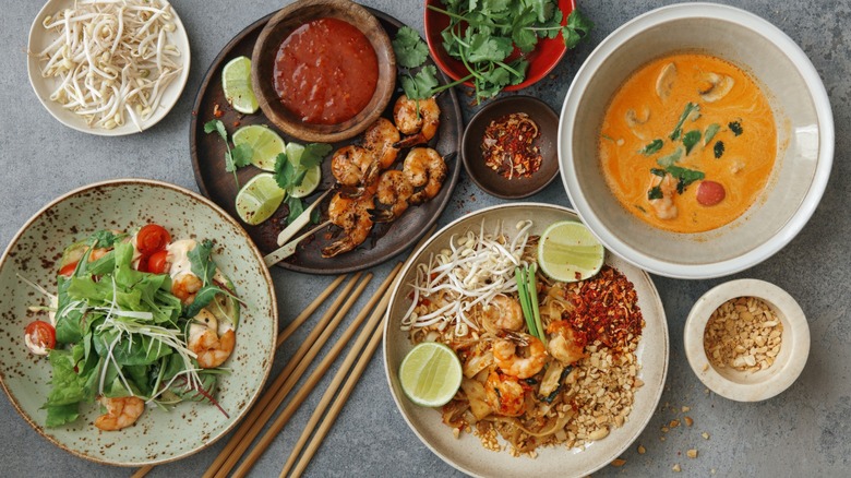 Authentic classic Thai dishes including Pad Thai, curry, shrimp skewers, and a shrimp salad with aromatic garnishes and chopsticks