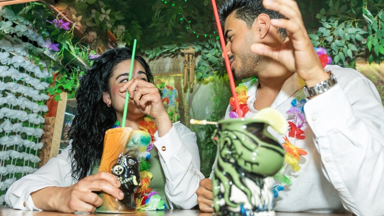 Young couple enjoying colorful tiki cocktails at a tropical-themed bar