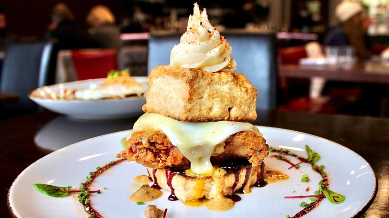 A brunch plate at The Conche featuring a biscuit with fried chicken, egg, melted cheese, and chocolate sauce