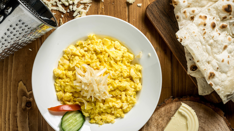 Scrambled eggs topped with shredded cheese, next to a cheese grater and tortillas