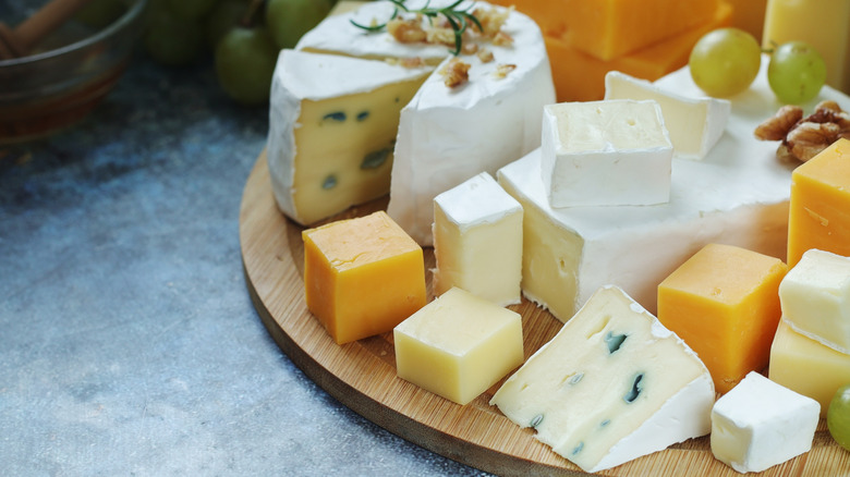 A closeup of a variety of soft and hard cheeses on a wooden platter