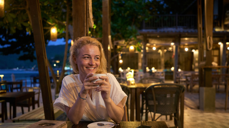 Happy woman day dreaming while drinking coffee during summer night in a beach restaurant