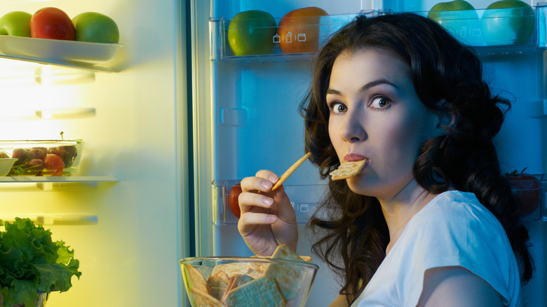 Woman eating crackers in front of open fridge