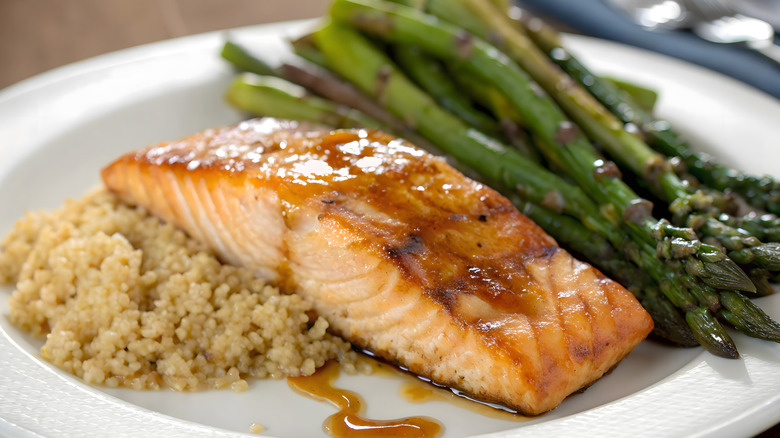 Filet of glazed salmon on plate next to quinoa and roasted asparagus