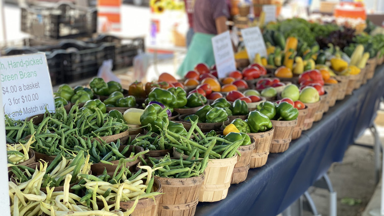 Baskets of fresh produce are laid out on a farmers market table with a sign advertising the price