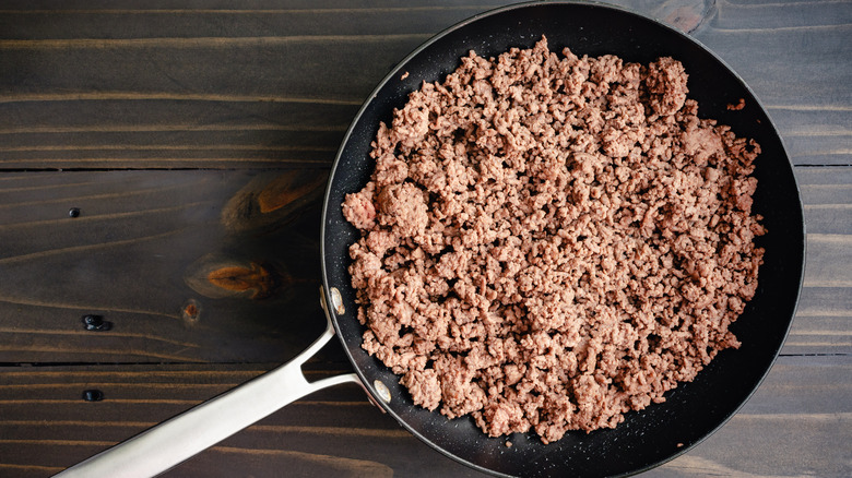 Cooked ground beef in a large non-stick frying pan on a wooden table.