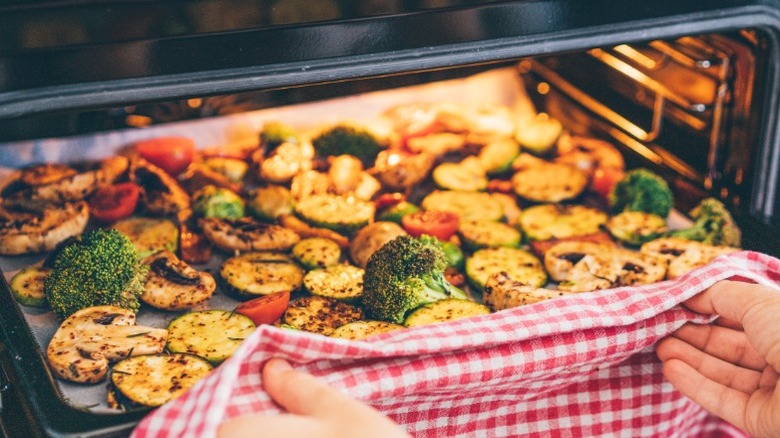 Hands pulling tray of veggies out of an oven.