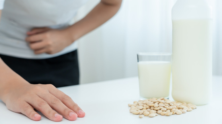 Soy beans and soy milk in a glass and container with person who has upset stomach in background