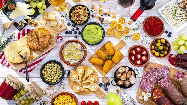 Overhead view of a white table filled with delicious tapas, two beer glasses, and red wine.