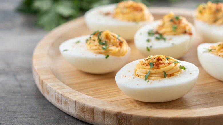 side profile photo of a plate full of deviled eggs with green onion and paprika garnish