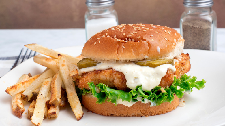 fried cod sandwich with creamy sauce, lettuce, pickles, and fries