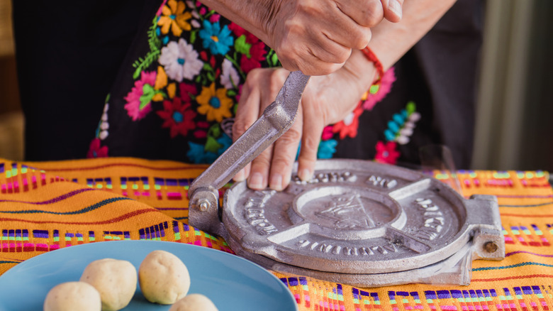 Woman in traditional Mexican clothes presses homemade corn tortillas on a press