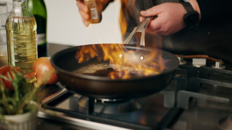 A close-up of flamb&eacute; cooking in a skillet pan on a stovetop with a man's hands