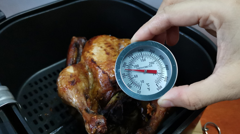 A hand inserts a meat thermometer into a chicken in an air fryer