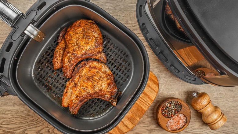 Two pork chops in an air fryer on a wooden surface