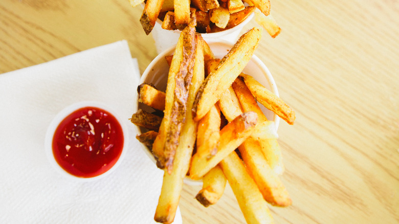 Fries in a cup next to ketchup on a wood table.
