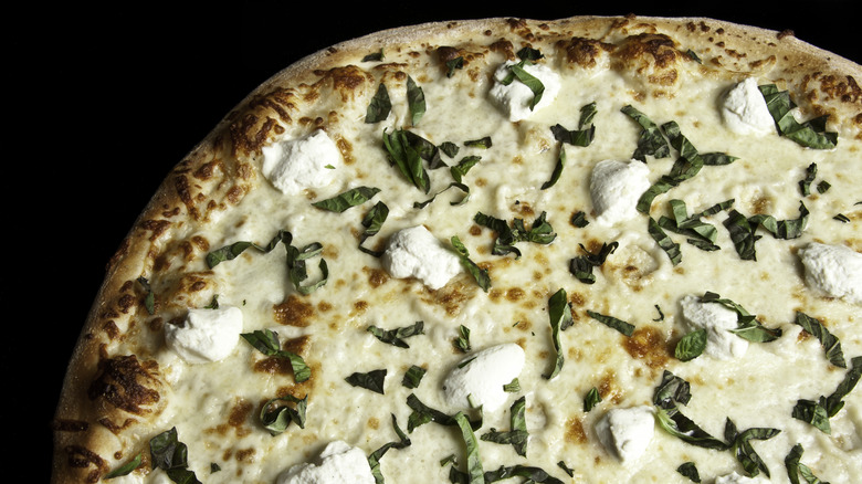 White pizza with dollops of ricotta and fresh basil sprinkled on top.