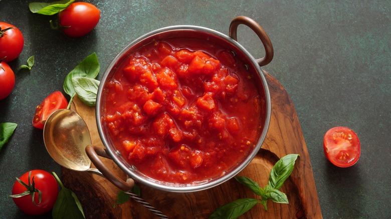 Tomato sauce in pot with whole tomatoes and basil nearby