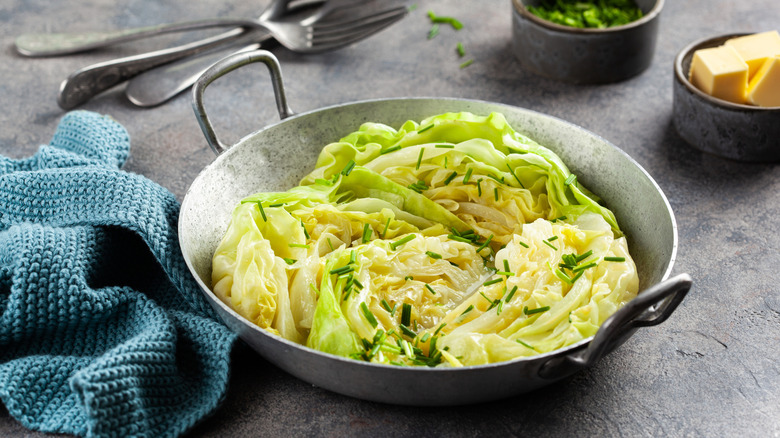 cooked cabbage in a metal pot next to a crumpled blue towel